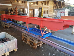 MATEC Vibrorinne Antrieb 3 hinten, Standardbreite 600 mm, Höhe 260 mm, Länge 7 m, 2-teiliger Bodenrahmen zur Durchführung der Rinne durch ein Betonfundament unter einer Blockbandsäge, Materialabgabe nach unten in Folgeförderanlage, Ueberlängen-Aussiebung mit Abwurf nach vorne